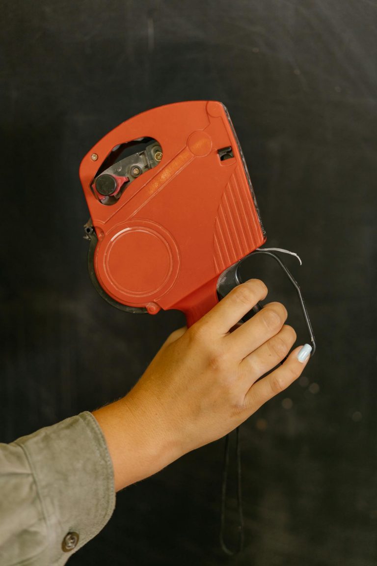 A person holds a red price tag gun, ideal for labeling and pricing in retail settings.